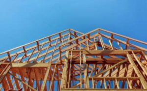 looking up at a wood frame of a new home construction project with clear blue sky behind