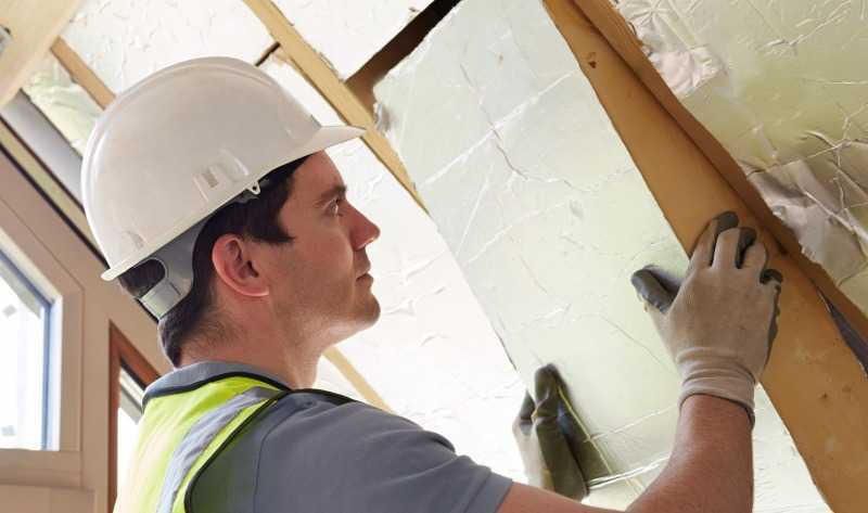 Worker in hardhat installing attic insulation with foil facing.