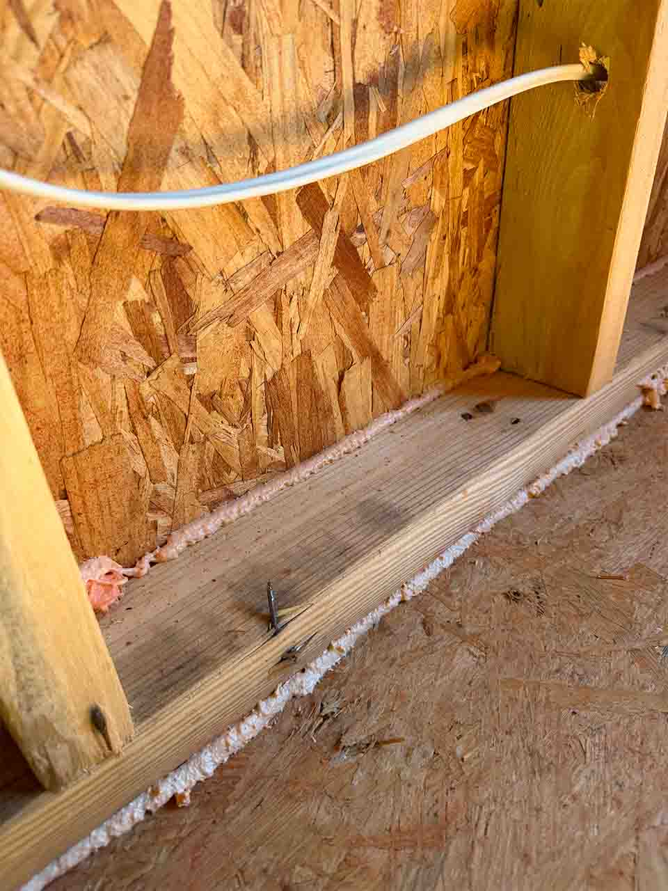 Spray foam sealant air sealing a bottom plate seam and wire penetration in a new construction DRB Homes home in Stockbridge, GA by Foster Insulation.