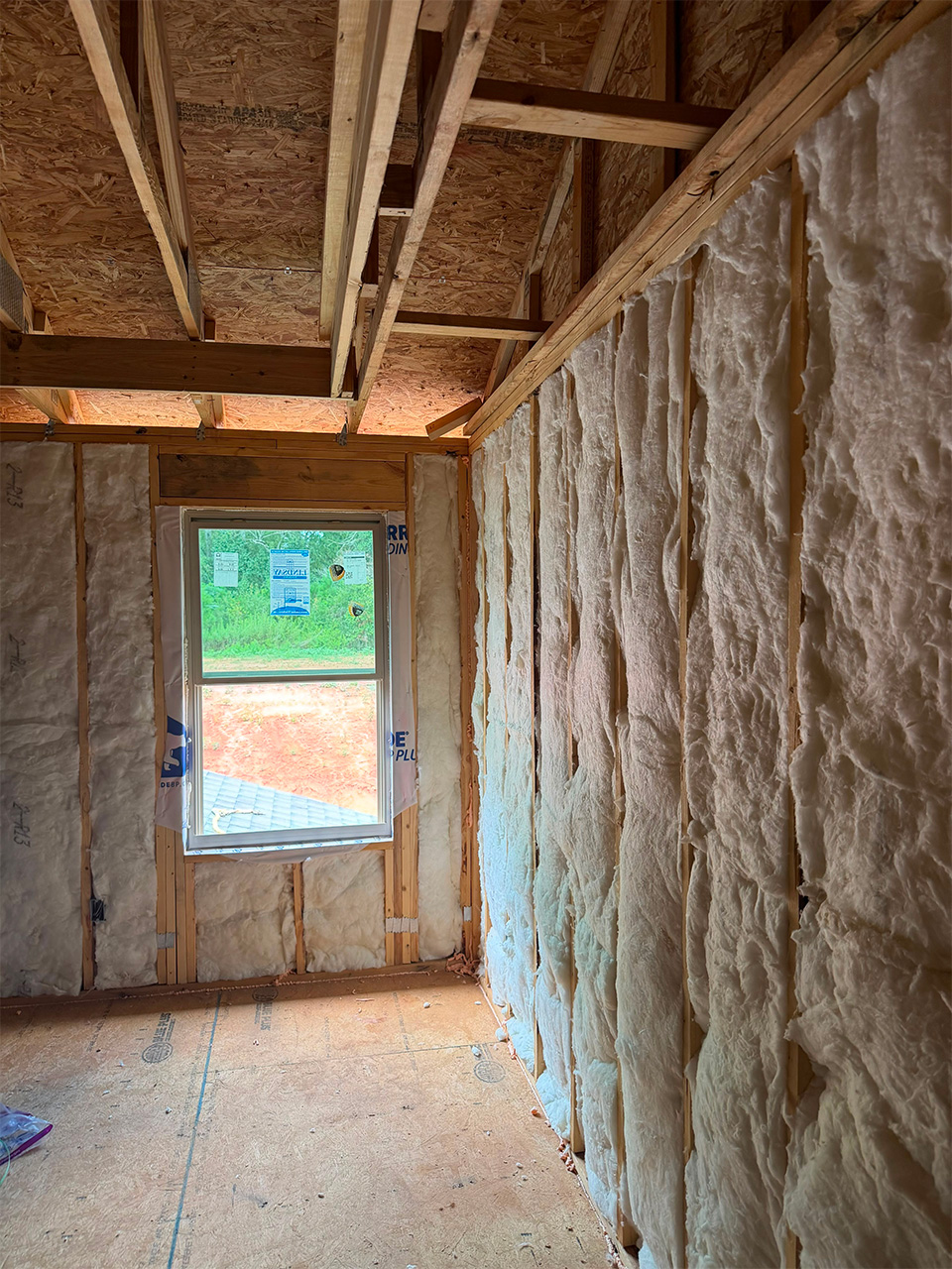 Fiberglass batt wall insulation installed along a corner wall and window in a framed DRB Homes new construction home in Stockbridge, GA by Foster Insulation.