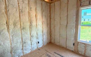Fiberglass batt wall insulation installed in a corner room with a window overlooking neighboring homes at Kingston Park in Kingston, GA for Smith Douglas Homes.
