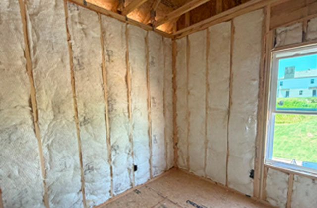 Fiberglass batt wall insulation installed in a corner room with a window view of neighboring homes at Kingston Park in Kingston, GA for Smith Douglas Homes.