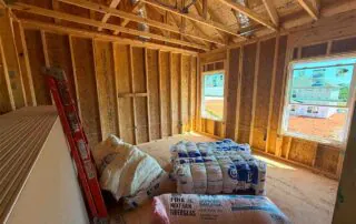 Bundles of Johns Manville and Owens Corning fiberglass batt insulation staged on a subfloor at Kingston Park in Kingston, GA for Smith Douglas Homes.