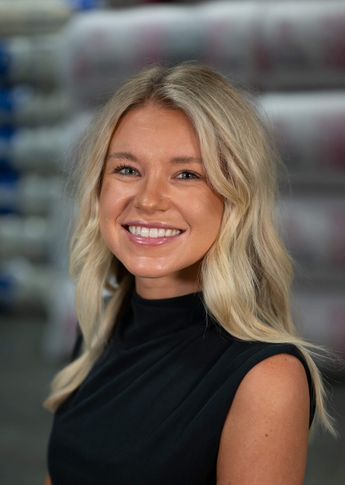 Amber Luck Amber Luck smiling in a professional setting, wearing a black top with a blurred background of insulation materials