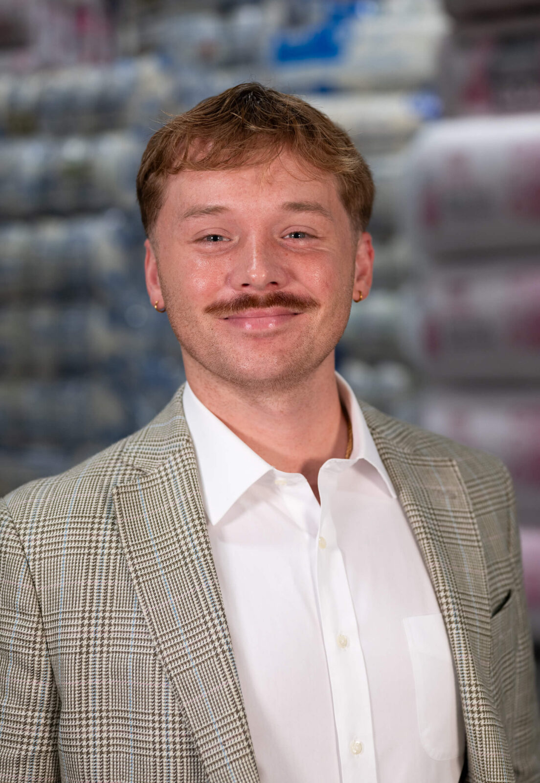 Jalen Luck Jalen Luck smiling, wearing a plaid blazer and white shirt, standing in front of blurred insulation products