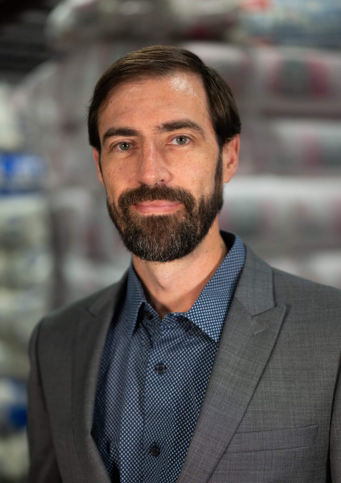 Ryan Ryan in a gray suit with a patterned blue shirt, standing in front of stacked insulation materials, indoor setting