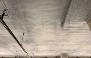Closed-cell spray foam insulation along a parking deck ceiling and concrete block wall in Fulton County, GA.