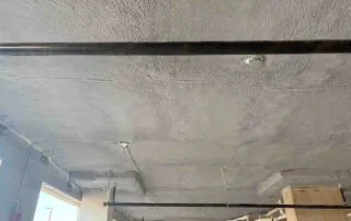 Closed-cell spray foam covering a parking deck ceiling above a dense plumbing and conduit network in Fulton County, GA.