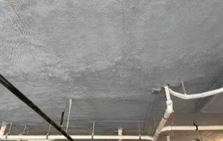 Closed-cell spray foam applied over a parking deck ceiling with PVC pipe runs in Fulton County, GA.