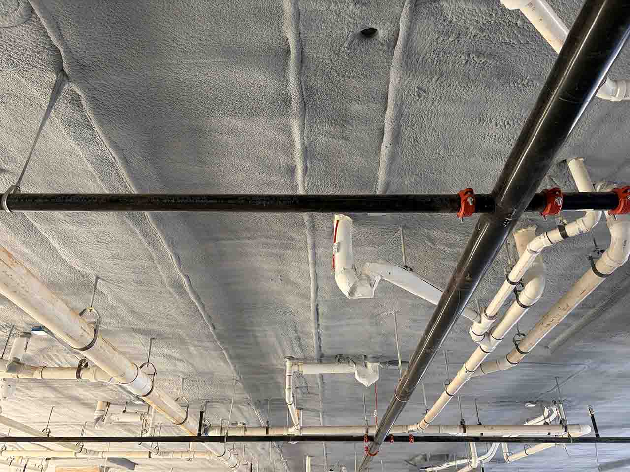 Closed-cell spray foam sealed around plumbing pipe penetrations on a parking deck ceiling in Fulton County, GA.