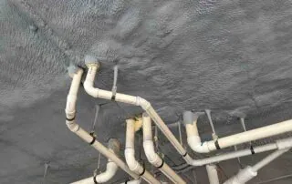 Closed-cell spray foam sealed around plumbing pipe penetrations on a parking deck ceiling in Fulton County, GA.