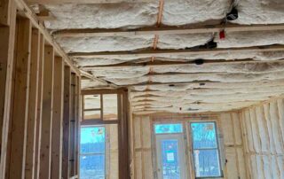Foster Insulation fiberglass batt insulation installed between ceiling joists and in the exterior walls of an open living area under construction.