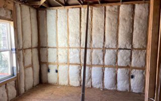 Fiberglass batt insulation installed in the wood stud walls of a room beside a window.