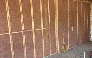 Spray-applied cellulose insulation filling wood stud wall cavities in a residential remodel.